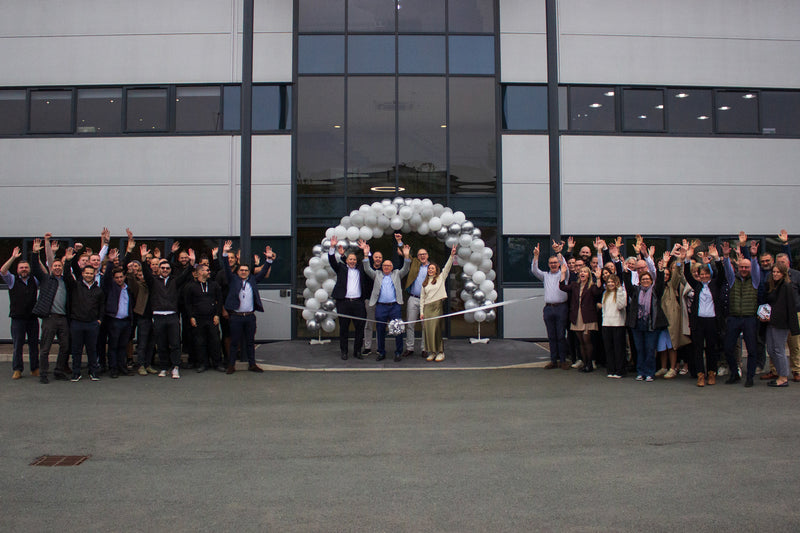 Group of people at a ribbon-cutting ceremony in front of a modern building with balloons.