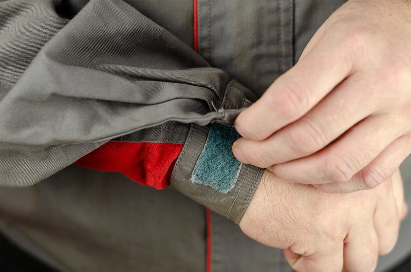 adjusting a wrist hook and loop strap on a grey and red jacket