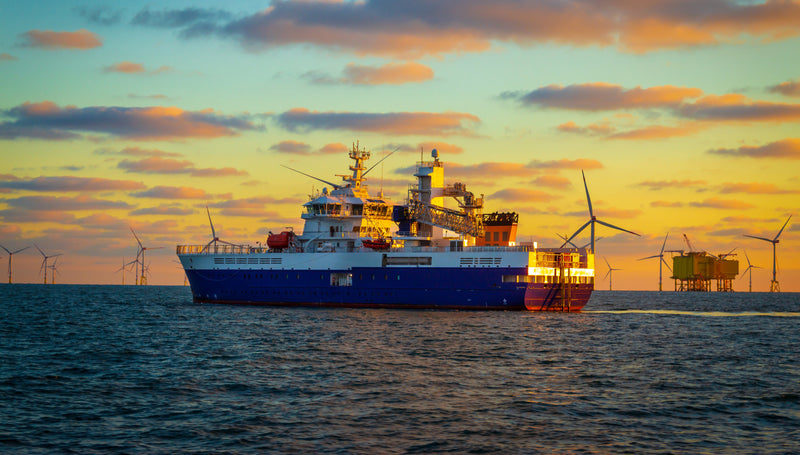 a industrial ship naviagting its way across the ocean surrounded by wind turbines