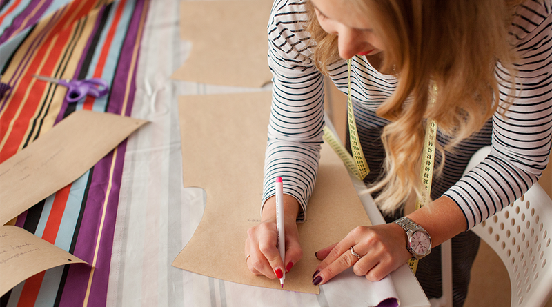 Seamstress marking a fabric pattern with a pen and tape measure on a workroom table